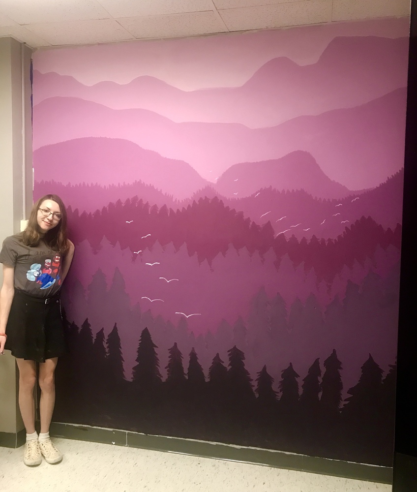Student standing next to mural on wall that she painted