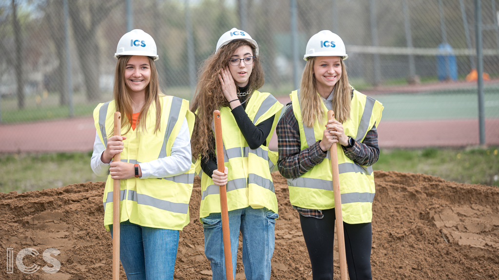 3 students in hard hats at the ground breaking holding shovels