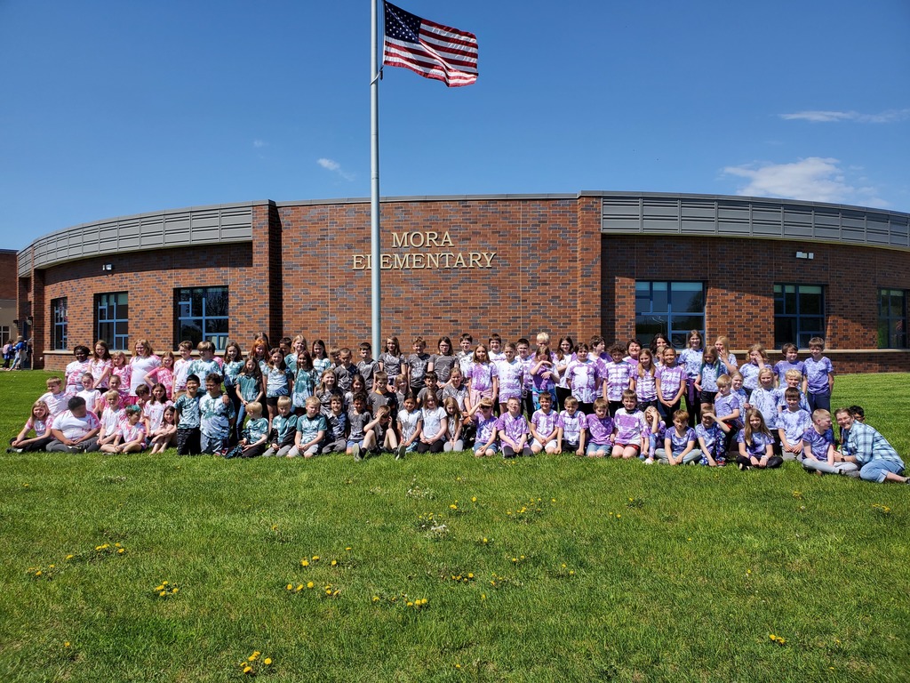 Photo of students wearing their tie dyed t-shirts in front of the elementary school, pink, purple, turquoise, gray colored shirts.
